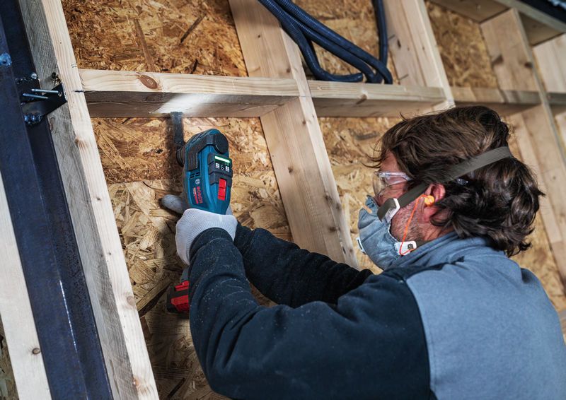 Une personne portant un équipement de sécurité utilise un coupe-bordures sans fil pour travailler sur une charpente en bois.