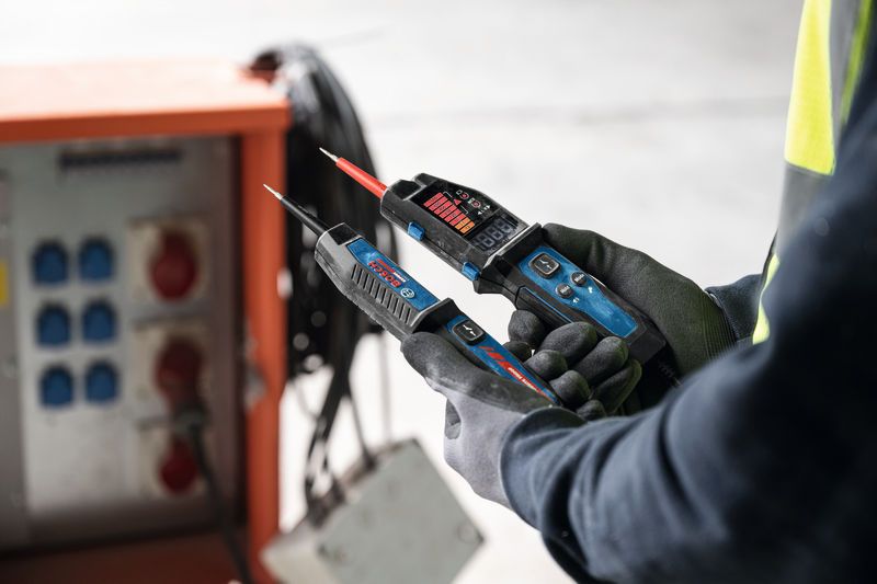 Une personne portant un équipement de sécurité utilise un testeur de tension à proximité d’un panneau électrique.