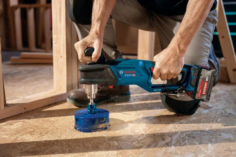 Une personne utilise une perceuse d’angle sans fil pour percer un grand trou dans un plancher en bois.