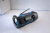 Radio de chantier portable avec écran et deux haut-parleurs, posée sur un sol en béton.