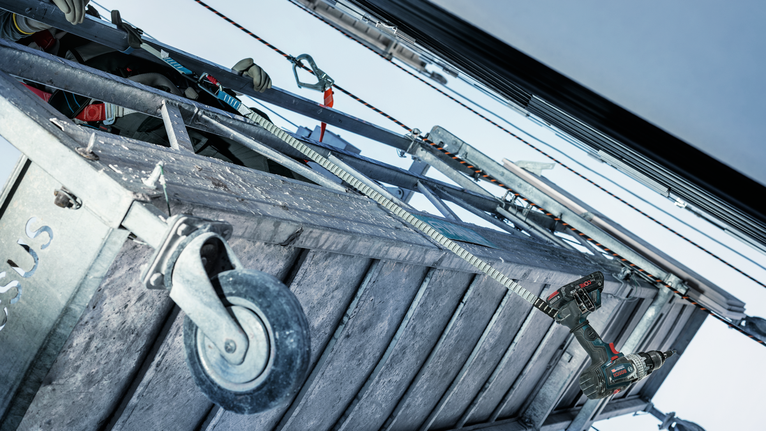 Une personne portant un équipement de sécurité utilise une perceuse sur une structure métallique.