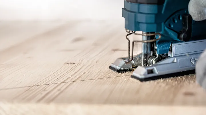 Une personne guide une scie sauteuse le long d'une ligne marquée pour couper une planche de bois.