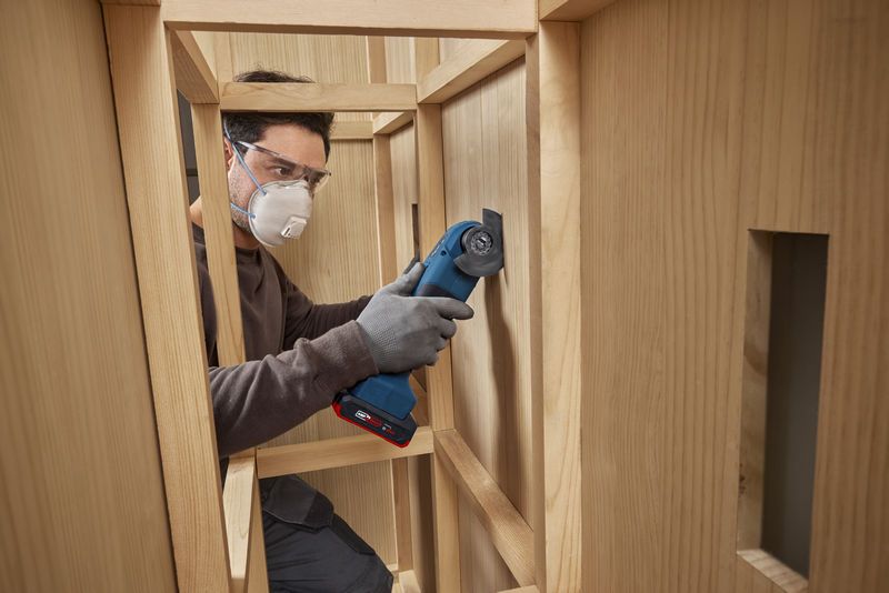 Une personne portant un équipement de sécurité utilise un outil multifonction pour couper du bois à l’intérieur d’une armoire.