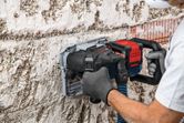 Une personne portant un équipement de sécurité utilise une rainureuse pour découper des rainures dans un mur en béton.