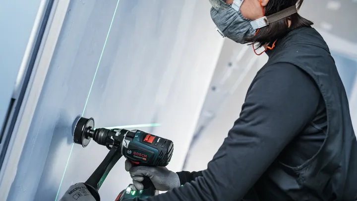 Une personne portant un équipement de sécurité perce un mur à proximité d'un guide laser vert.