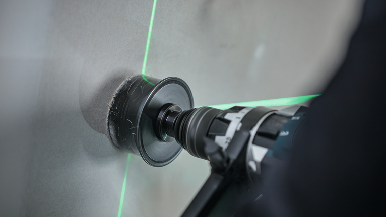 Une personne utilise une perceuse électrique avec une scie cloche pour couper des carreaux, guidée par des lignes laser vertes.