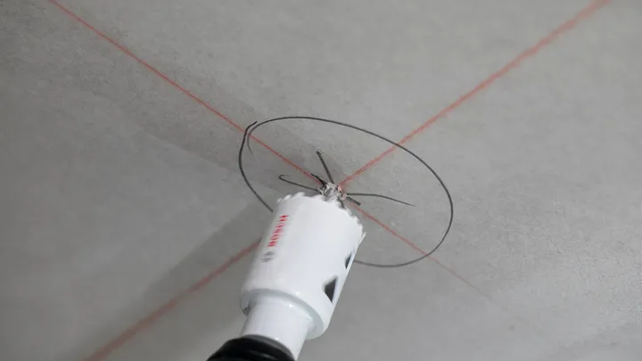 Perçage à la scie cloche d'une ouverture circulaire sur un plafond marqué de lignes de guidage rouges.