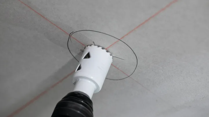 Perçage d'une coupe circulaire à la scie cloche dans un plafond marqué de lignes de guidage rouges.
