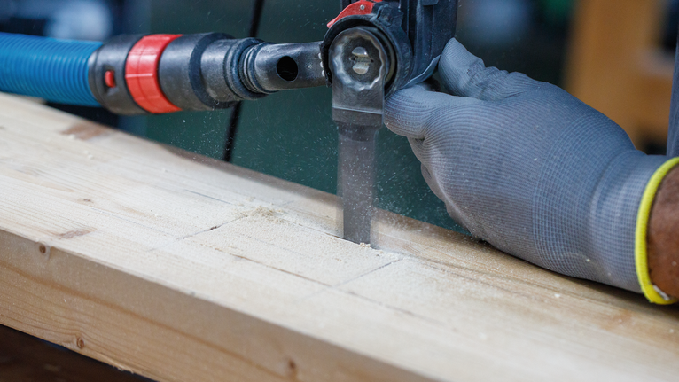Une personne portant un équipement de sécurité coupe une planche de bois avec une scie alternative.