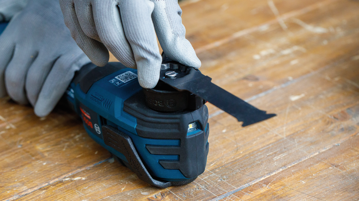 Une personne portant un équipement de sécurité ajuste un outil multifonction sur une surface en bois.