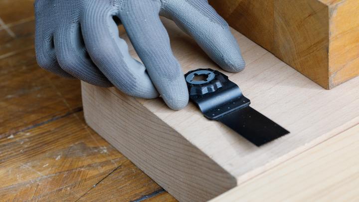 Une personne portant un équipement de sécurité positionne une lame d'outil multifonction sur une surface en bois.