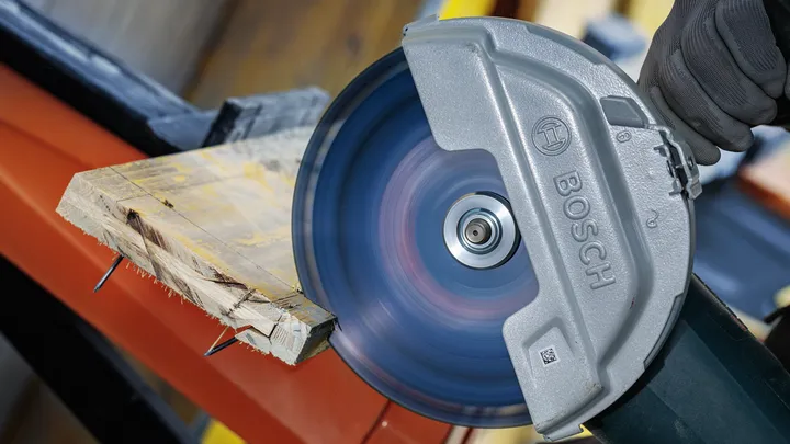 Une personne portant un équipement de sécurité utilise une scie circulaire pour couper une planche de bois.