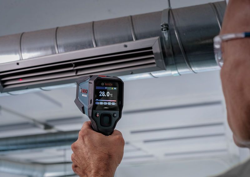 Une personne utilise un détecteur thermique pour mesurer la température dans une gaine de ventilation.