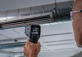 Une personne utilise un détecteur thermique pour mesurer la température dans une gaine de ventilation.