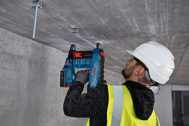 Une personne portant un équipement de sécurité fixe un cintre métallique à un plafond en béton.