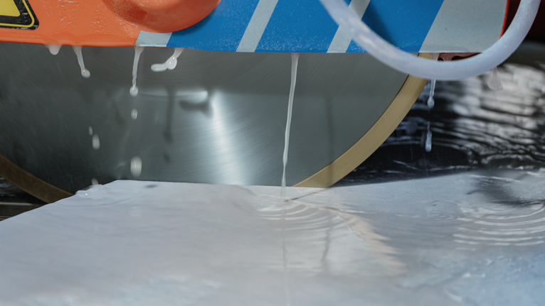Une scie circulaire à refroidissement par eau coupe un carreau blanc lisse.