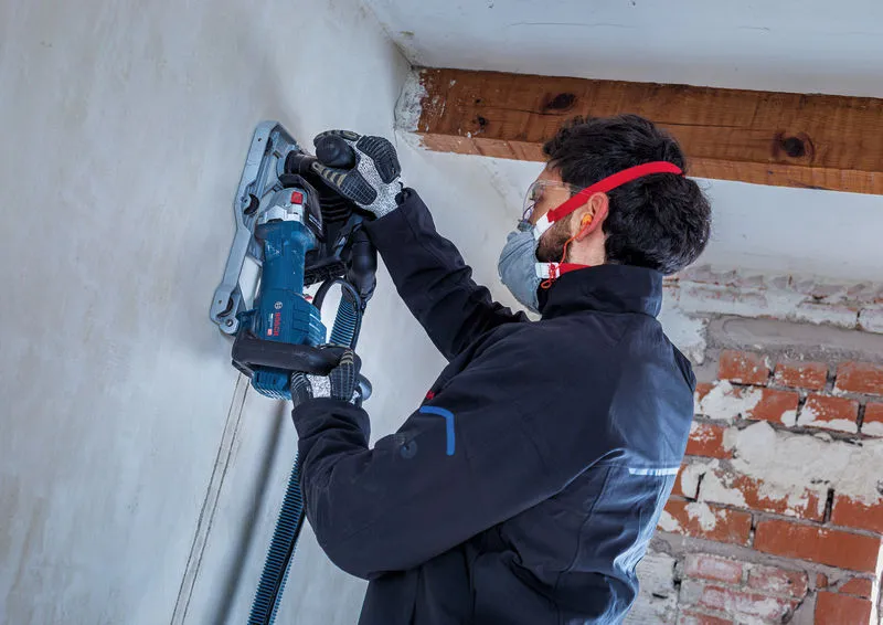 Une personne portant un équipement de sécurité utilise une rainureuse pour découper une rainure dans le plâtre.