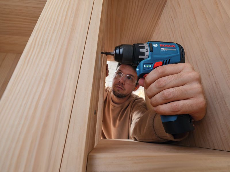 Une personne portant un équipement de sécurité utilise une perceuse-visseuse sans fil sur un cadre en bois.