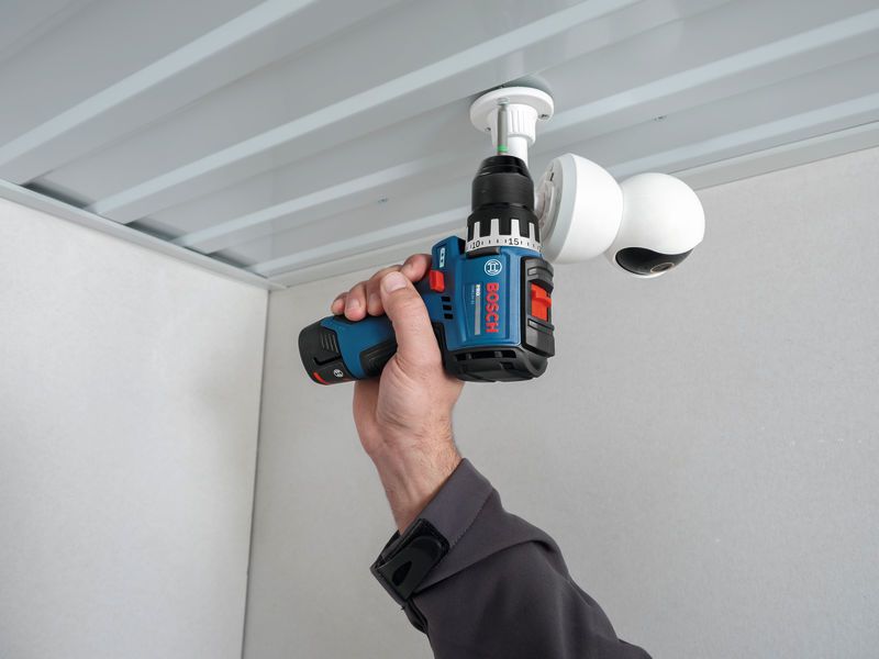 Une personne utilise une perceuse sans fil pour installer une caméra de sécurité au plafond.