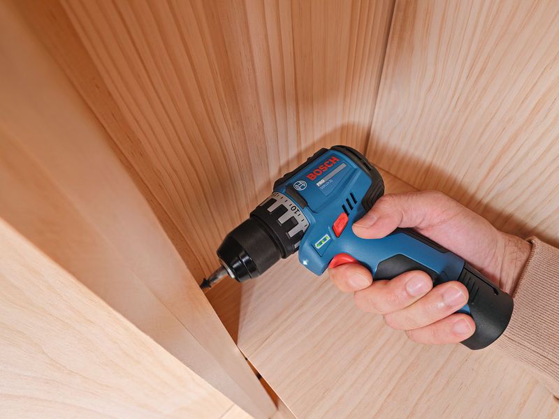 Une personne utilise une perceuse sans fil pour visser une vis dans une surface en bois.