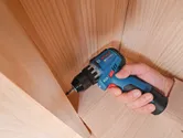 Une personne utilise une perceuse sans fil pour visser une vis dans une surface en bois.