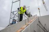 Une personne portant un équipement de sécurité utilise un outil électrique sur un escalier en béton sur un chantier de construction.