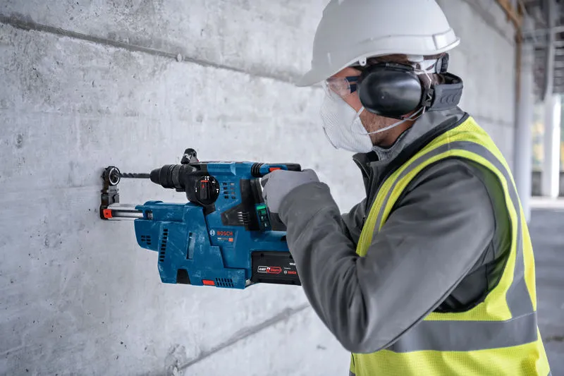 Un ouvrier portant un équipement de sécurité perce un mur en béton à l'aide d'un marteau perforateur.