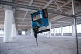 Perceuse à percussion sans fil suspendue à un échafaudage métallique à l'intérieur d'un grand bâtiment en construction.