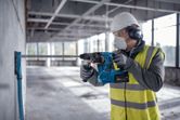 Une personne portant un équipement de sécurité perce un mur en béton avec un marteau perforateur.