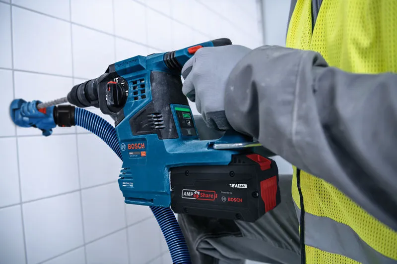 Une personne portant un équipement de sécurité utilise une perceuse à percussion sans fil contre un mur carrelé.
