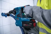 Une personne portant un équipement de sécurité utilise une perceuse à percussion sans fil contre un mur carrelé.