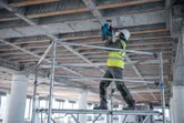 Une personne portant un équipement de sécurité perce un plafond en béton avec un marteau perforateur.