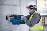 Une personne portant un équipement de sécurité perce un mur en béton avec un marteau perforateur.