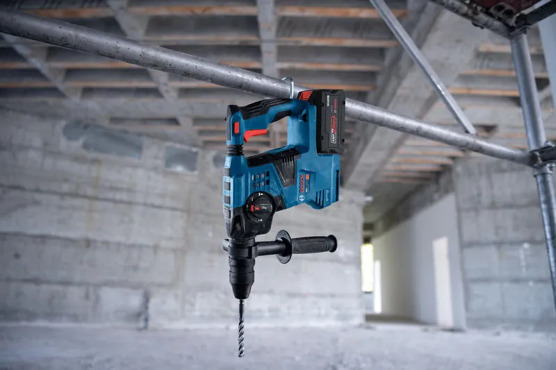 Marteau perforateur sans fil avec SDS plus, suspendu à un tuyau métallique sur un chantier de construction.