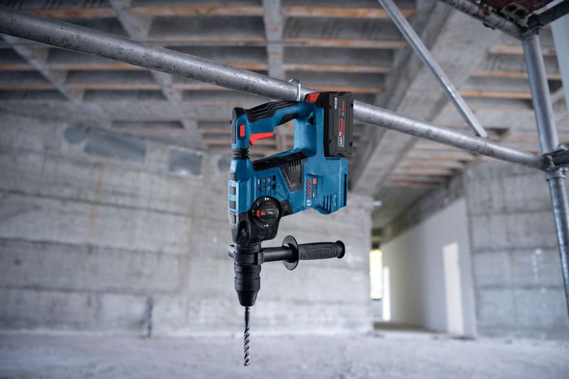 Marteau perforateur sans fil avec SDS plus, suspendu à un tuyau métallique sur un chantier de construction.