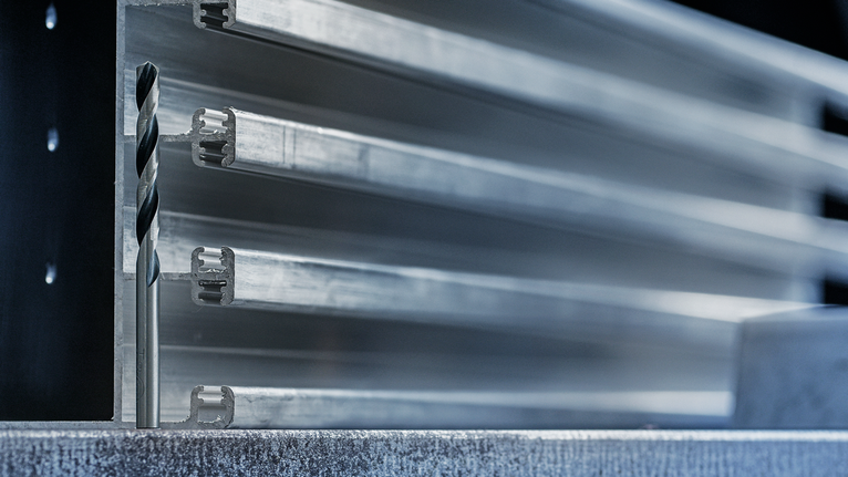 Foret à métaux positionné verticalement à côté de profilés en aluminium empilés.