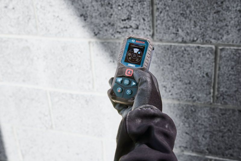 Une personne portant un équipement de sécurité utilise un télémètre laser près d'un mur en blocs de béton.