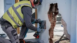 Une personne portant un équipement de sécurité utilise un outil électrique pour découper un mur en béton.