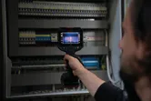 Une personne utilise une caméra thermique pour inspecter un tableau électrique.