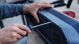 Une personne serre une vis sur un panneau de ventilation métallique à l'aide d'un tournevis.