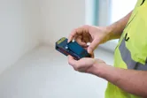 Une personne portant un équipement de sécurité utilise un télémètre laser dans une pièce vide.