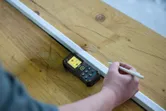 Une personne utilise un télémètre laser pour marquer une mesure sur une surface en bois.