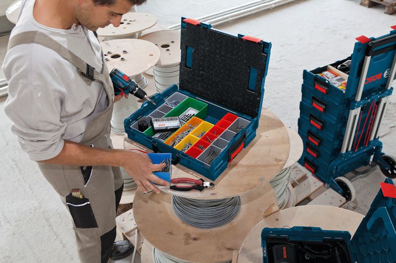 Une personne organise des attaches dans une boîte à outils sur une bobine de câble dans un atelier.