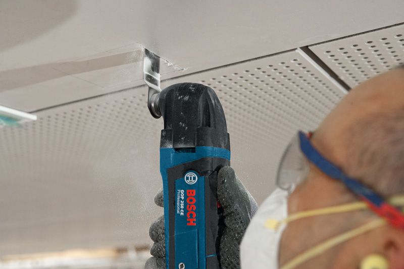 Une personne portant un équipement de sécurité utilise une pince coupante multifonction pour découper un panneau de plafond.