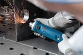 Une personne portant un équipement de sécurité meule un bord métallique avec un outil électrique, créant des étincelles.