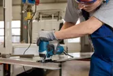 Une personne portant un équipement de sécurité coupe une feuille de métal à l’aide d’une scie sauteuse.