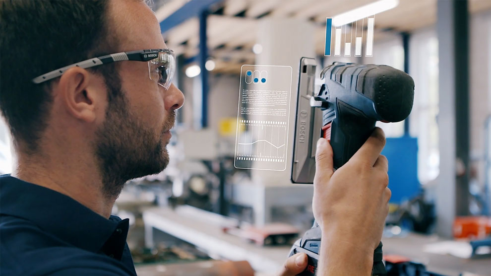 Een man met een bril houdt een Bosch-boormachine vast en kijkt naar een display.