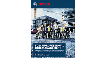 Des ouvriers en chantier posent devant un bâtiment, portant des casques jaunes et des gilets.