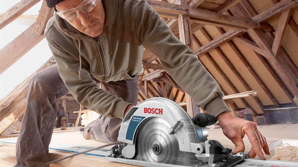Un homme utilise une scie circulaire Bosch dans un grenier en bois.