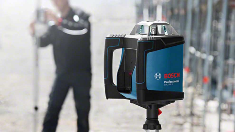 Een Bosch Professional laserwaterpas op een bouwplaats met een man op de achtergrond.